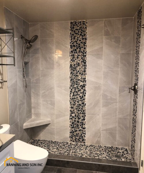 A gray mosaic tile shower with detachable shower head fixtures and a shower seat.