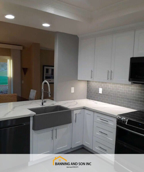 A gray-white kitchen with black appliances, a gray farmhouse sink and white countertops.