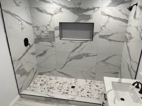 A gray tile shower with marbling and a gray hexagonal shower floor.