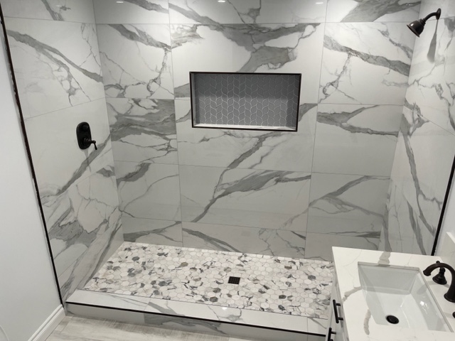 A gray tile shower with marbling and a gray hexagonal shower floor.