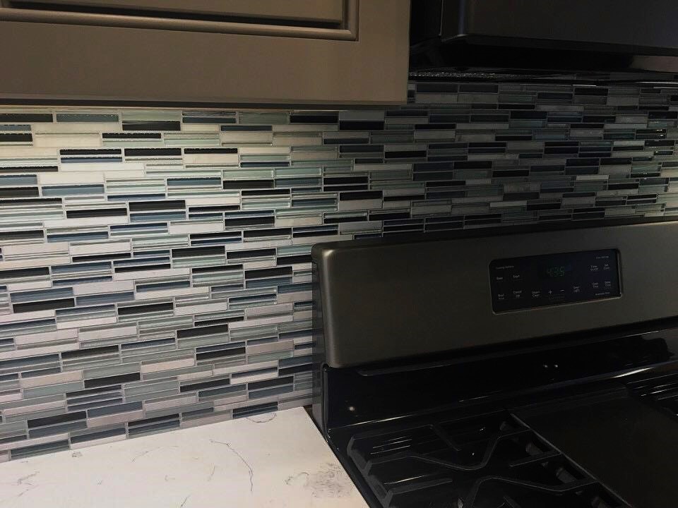 A kitchen with a sea glass tile backsplash behind a stove top.