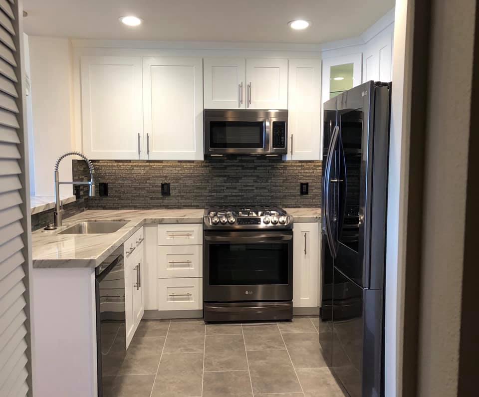 A small galley kitchen with darker tone appliances, beige countertops and a mosaic backsplash.