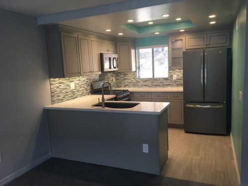A small galley kitchen with recessed lighting, blue accents and a mosaic sea glass backsplash.