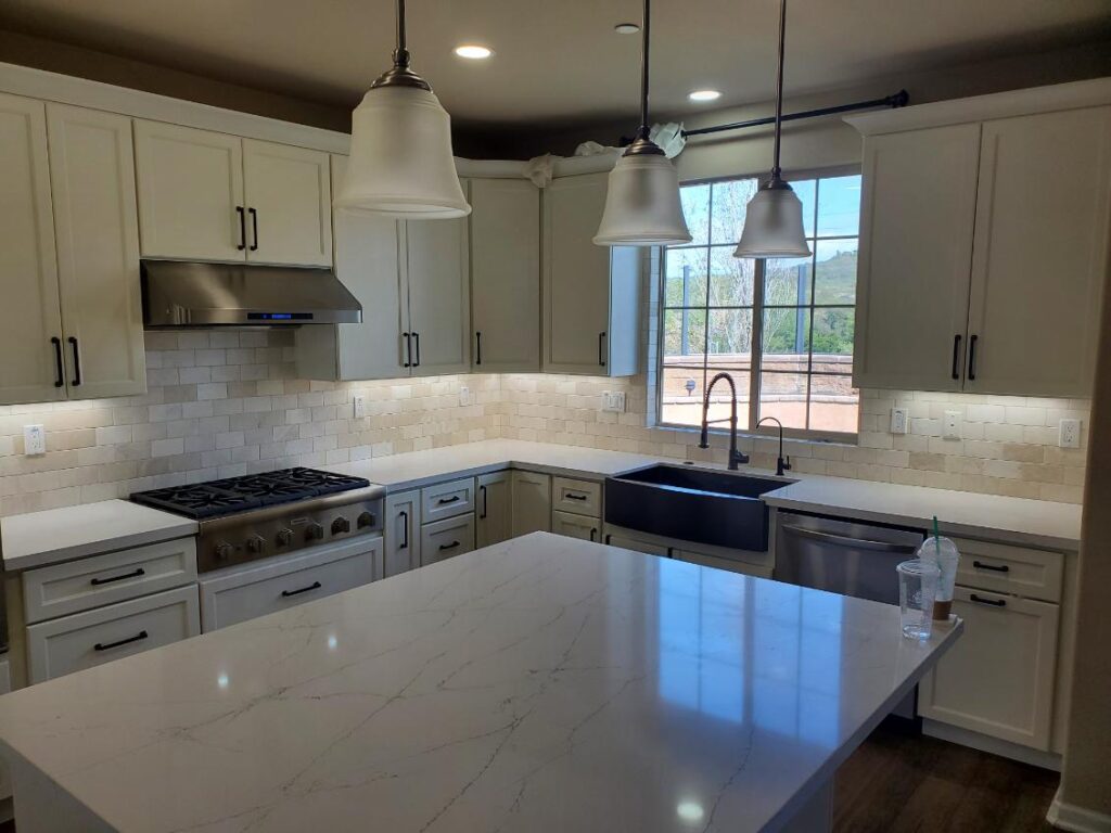 A kitchen with cream cabinets, white tile including the backsplash and pendant lighting.