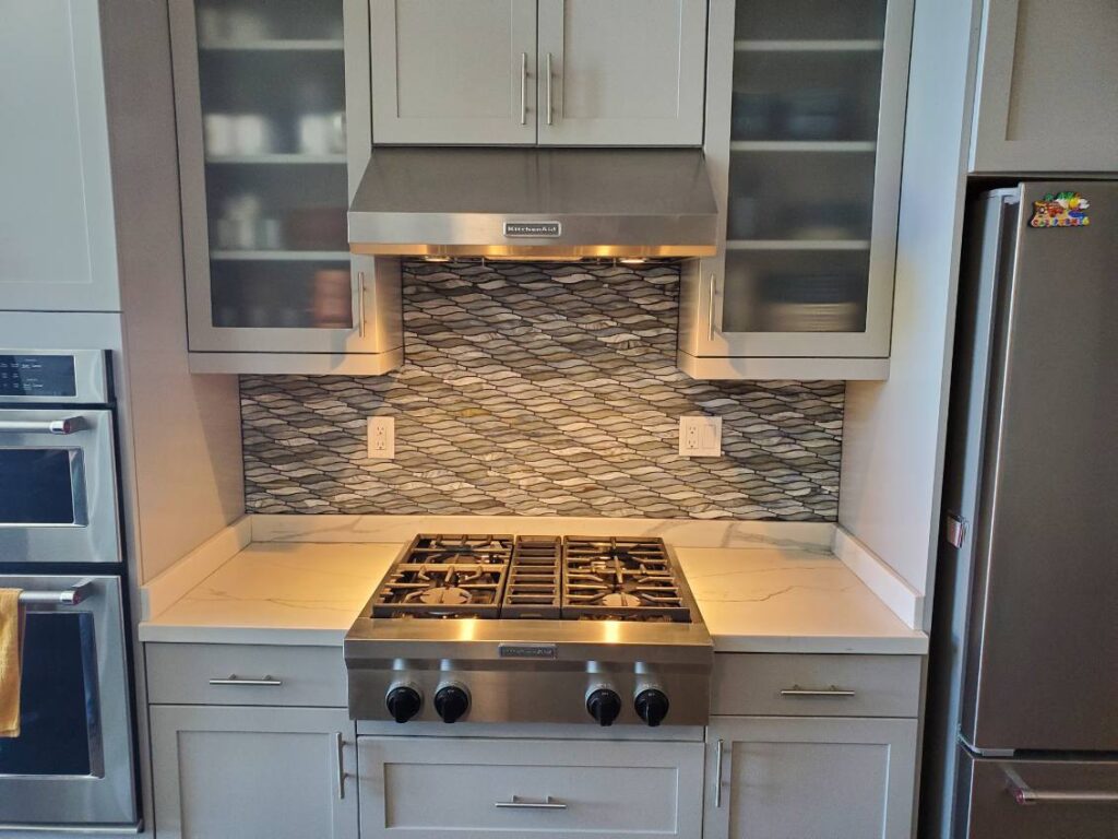 A kitchen with a KitchenAid gas range, white cabinets and a wavy backsplash.