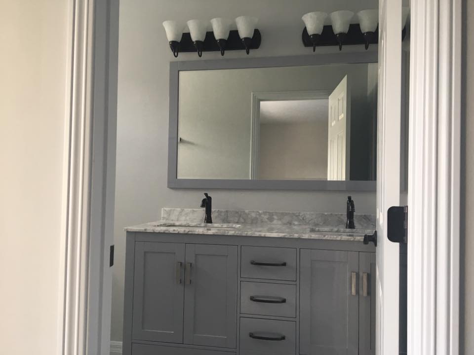 A gray bathroom with the double-sink vanity and mirror in focus. There are black vanity lights above the vanity.