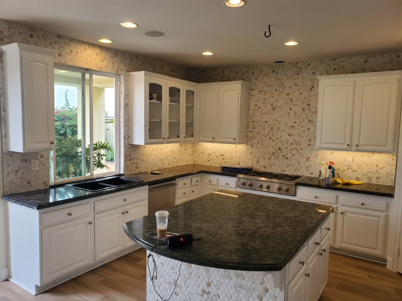 A kitchen with a mosaic beige tile with white cabinets and an island.