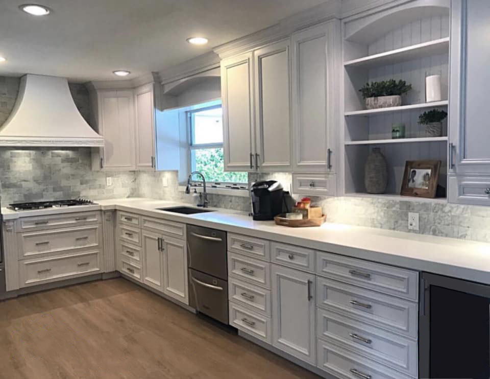 A gray kitchen with white raised-panel cabinets and drawers. Brand new appliances and a hardwood floor finish this beautiful kitchen remodel.