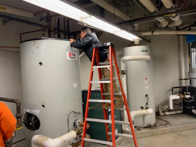 Adrian on a ladder inspecting a commercial-grade water heater.