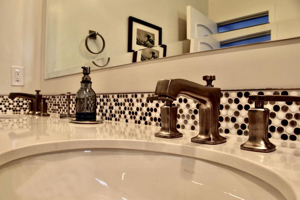 A brushed nickel bathroom faucet with a white-spotted backsplash.